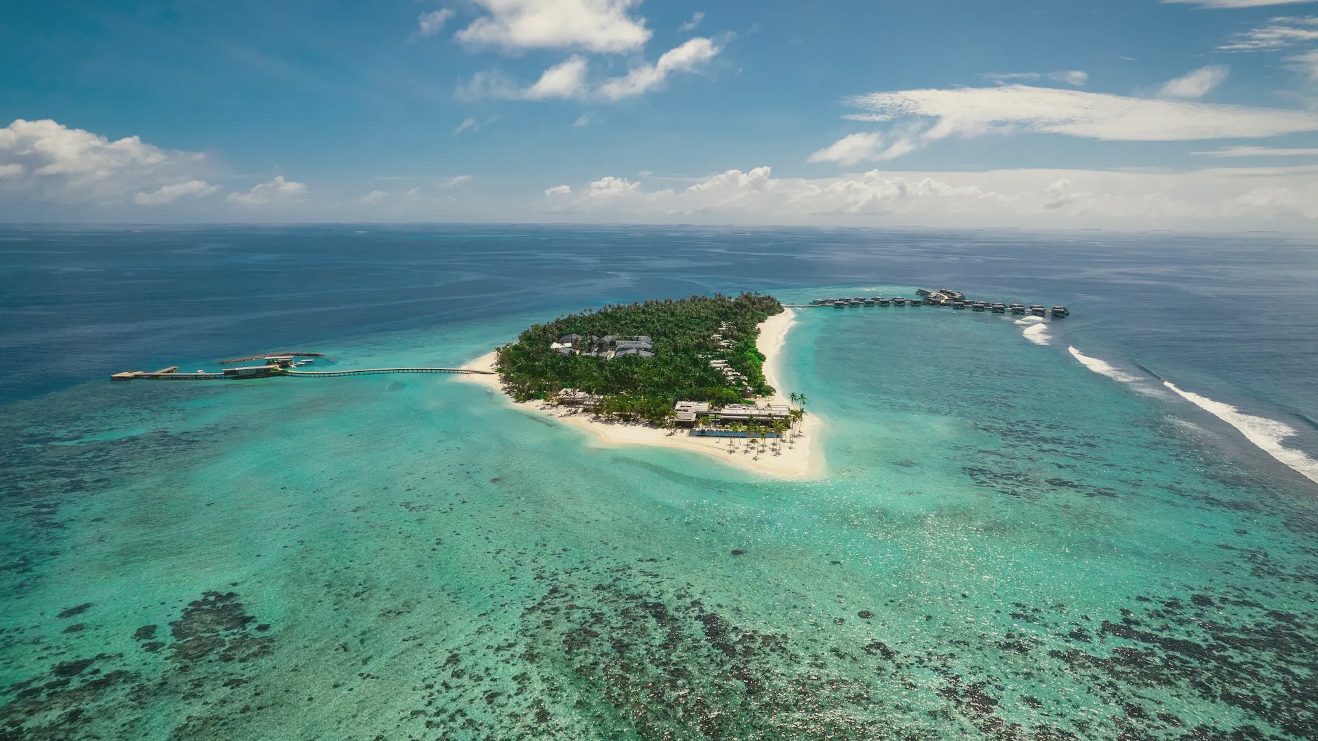 Kothaifaru from above. The island sits in Raa Atoll, its overwater villa jetties extending into the lagoon from a densely vegetated private island.