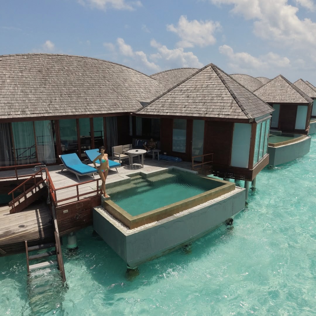 An overwater suite extending above the lagoon, the deck and private access steps visible against clear shallow water.