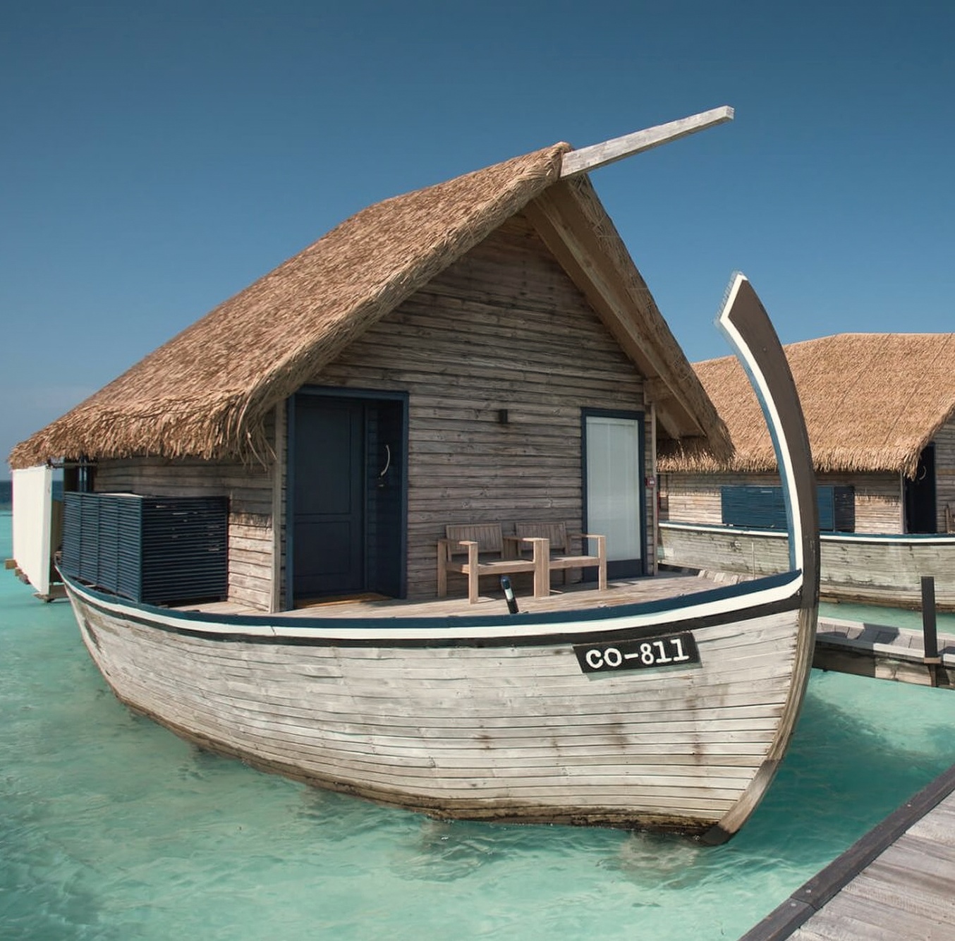 A dhoni villa exterior at water level. The curved hull profile and thatched roof distinguish the architecture from the standard overwater box found elsewhere in the atoll.