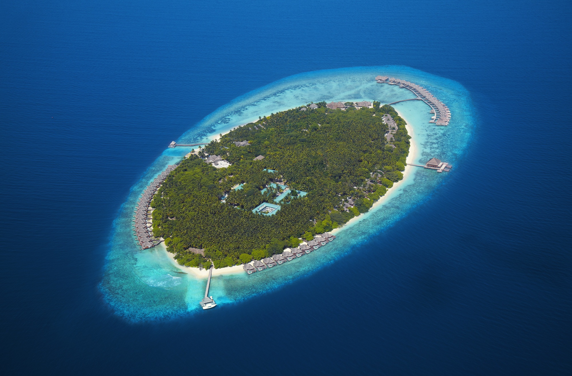 Mudhdhoo Island from above. The resort occupies its own island in the Baa Atoll UNESCO Biosphere Reserve, with beach and overwater villa wings visible from the air.