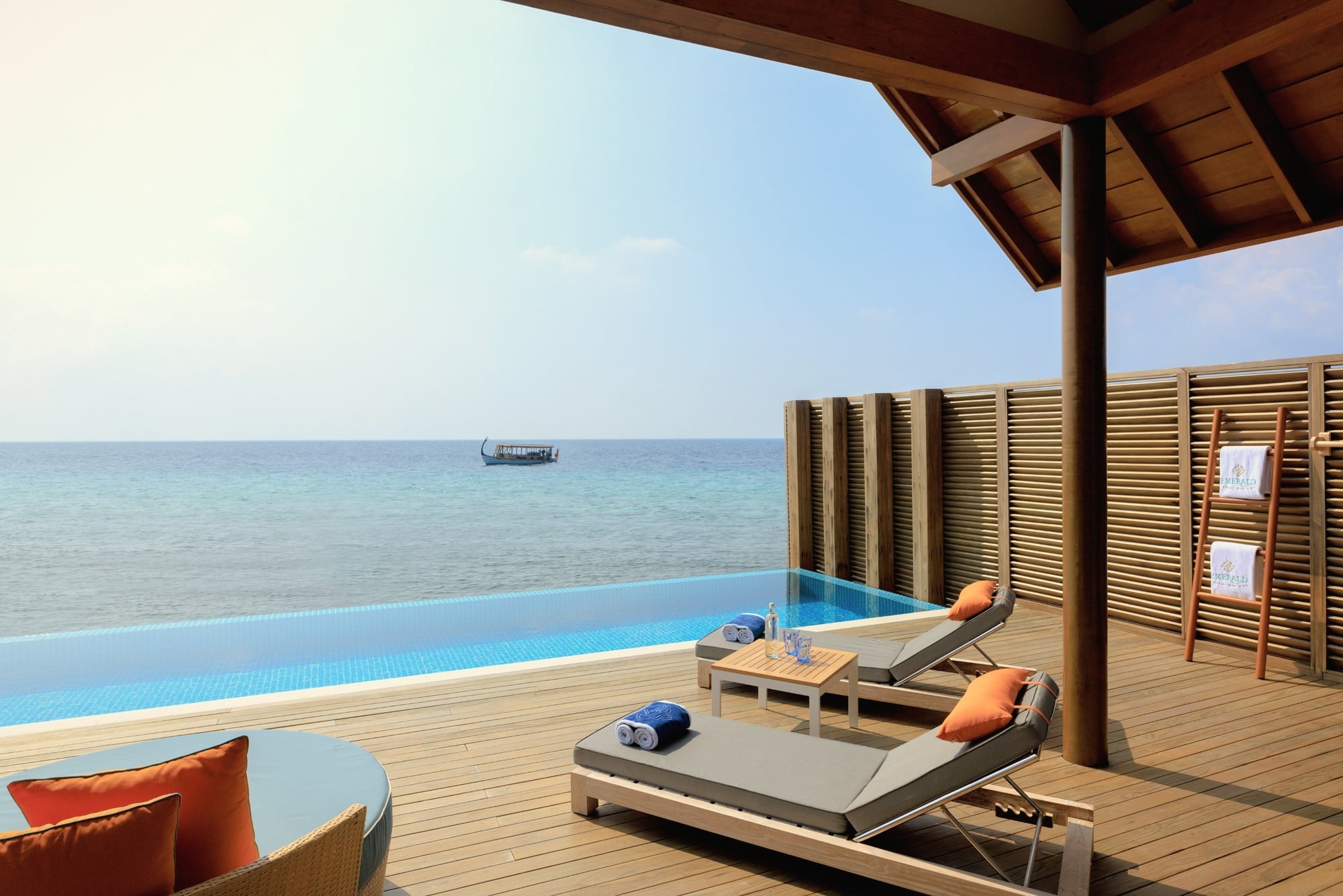 A water villa at the lagoon edge. The deck extends directly over the water, with steps down to the reef below.