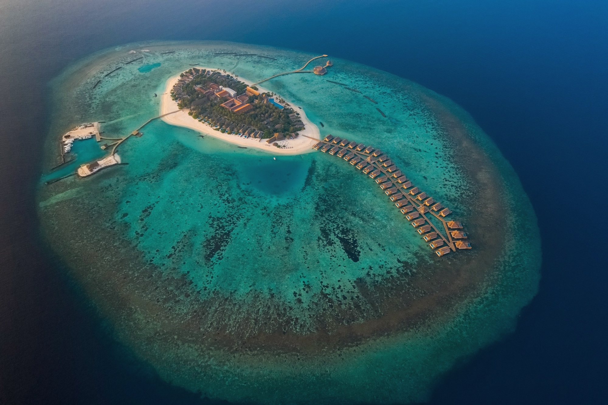 Faarufushi from above. The island sits alone in Raa Atoll, the overwater villa jetties extending into the lagoon on both sides.