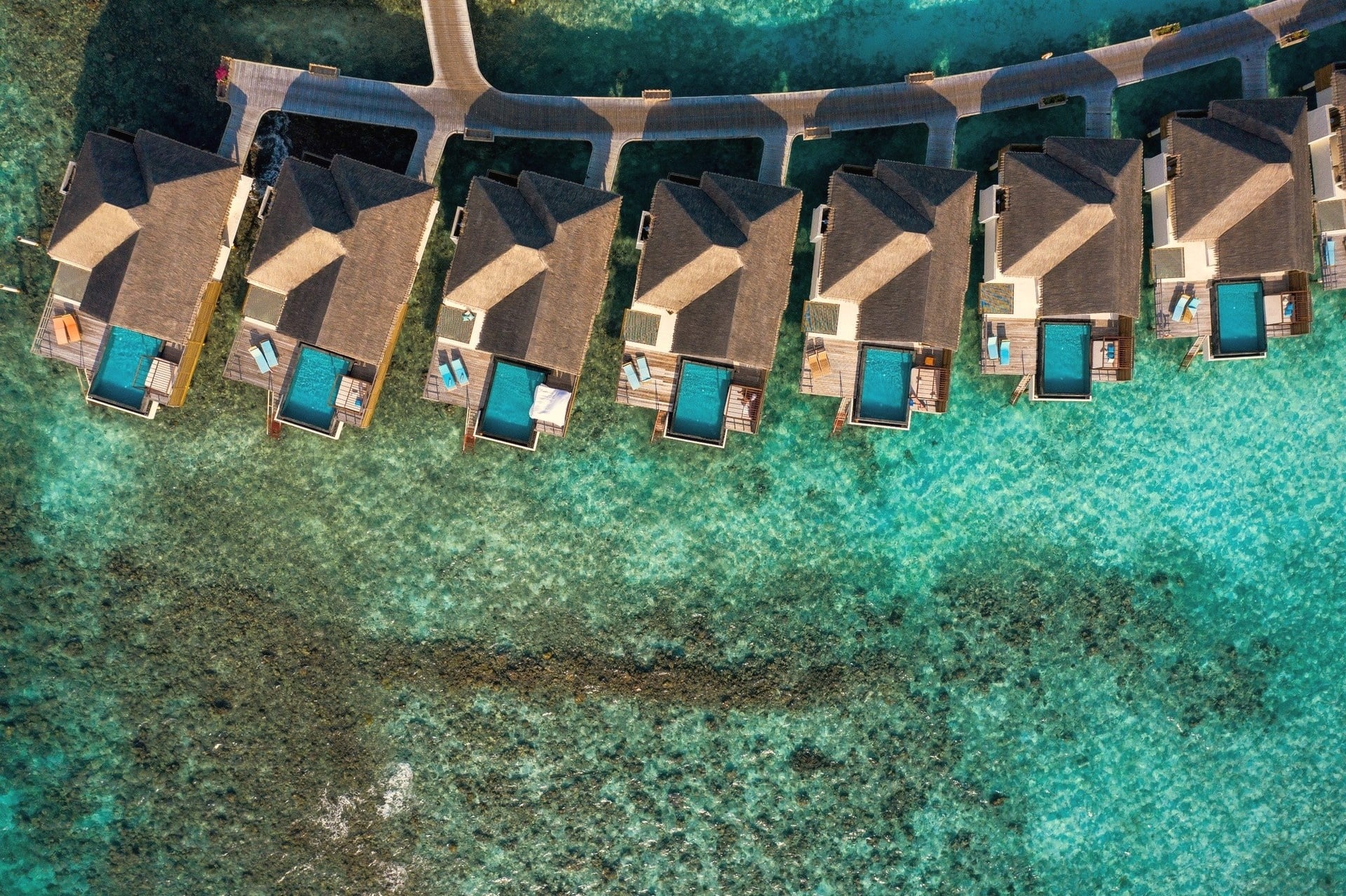 An overwater pool villa at the lagoon edge. The deck extends directly above the water, with the pool positioned to face the open ocean.