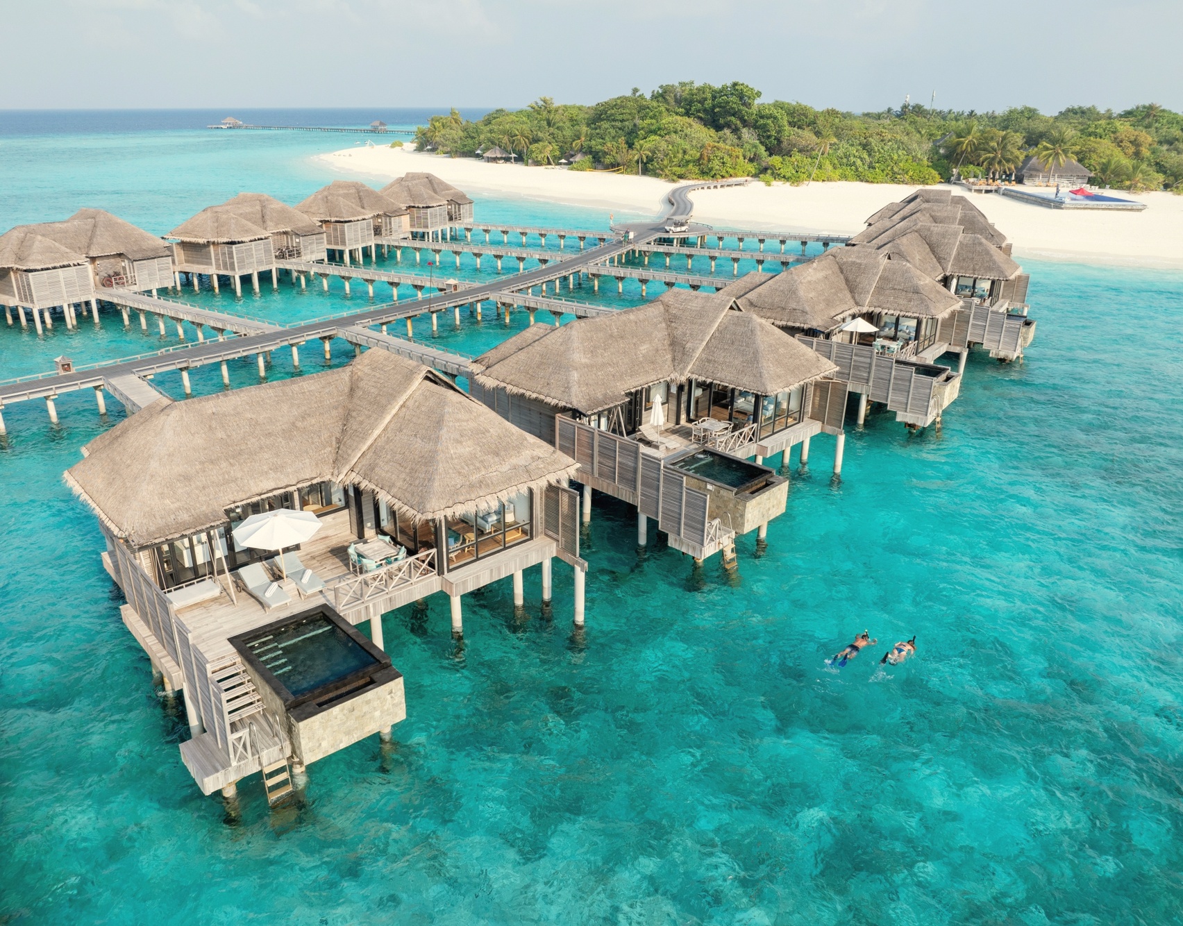 An overwater pool villa at dusk. The stilted structures extend over the lagoon, with direct water access from the deck.