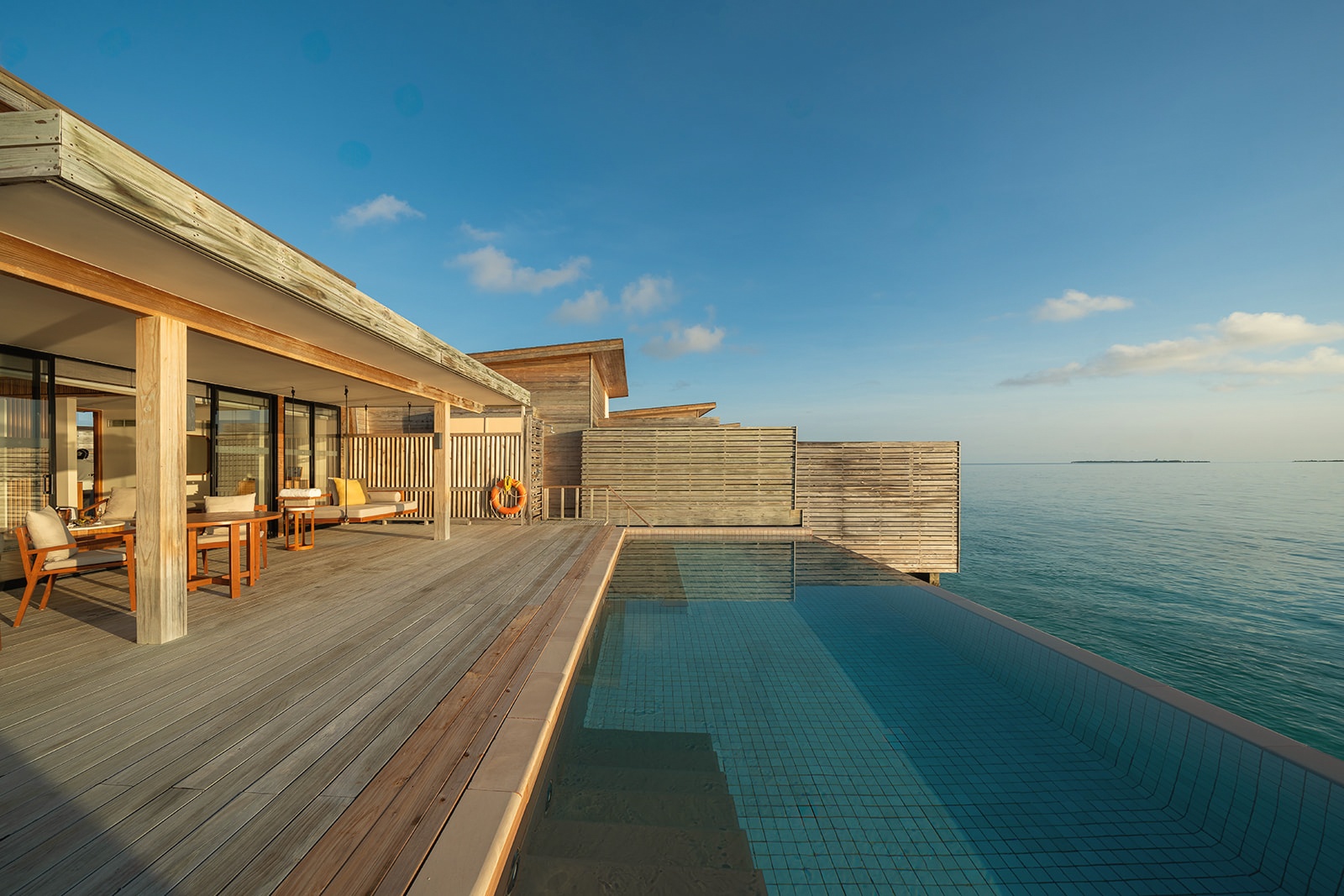 An overwater villa from the deck. The water is shallow and clear, the pool positioned at the lagoon edge.
