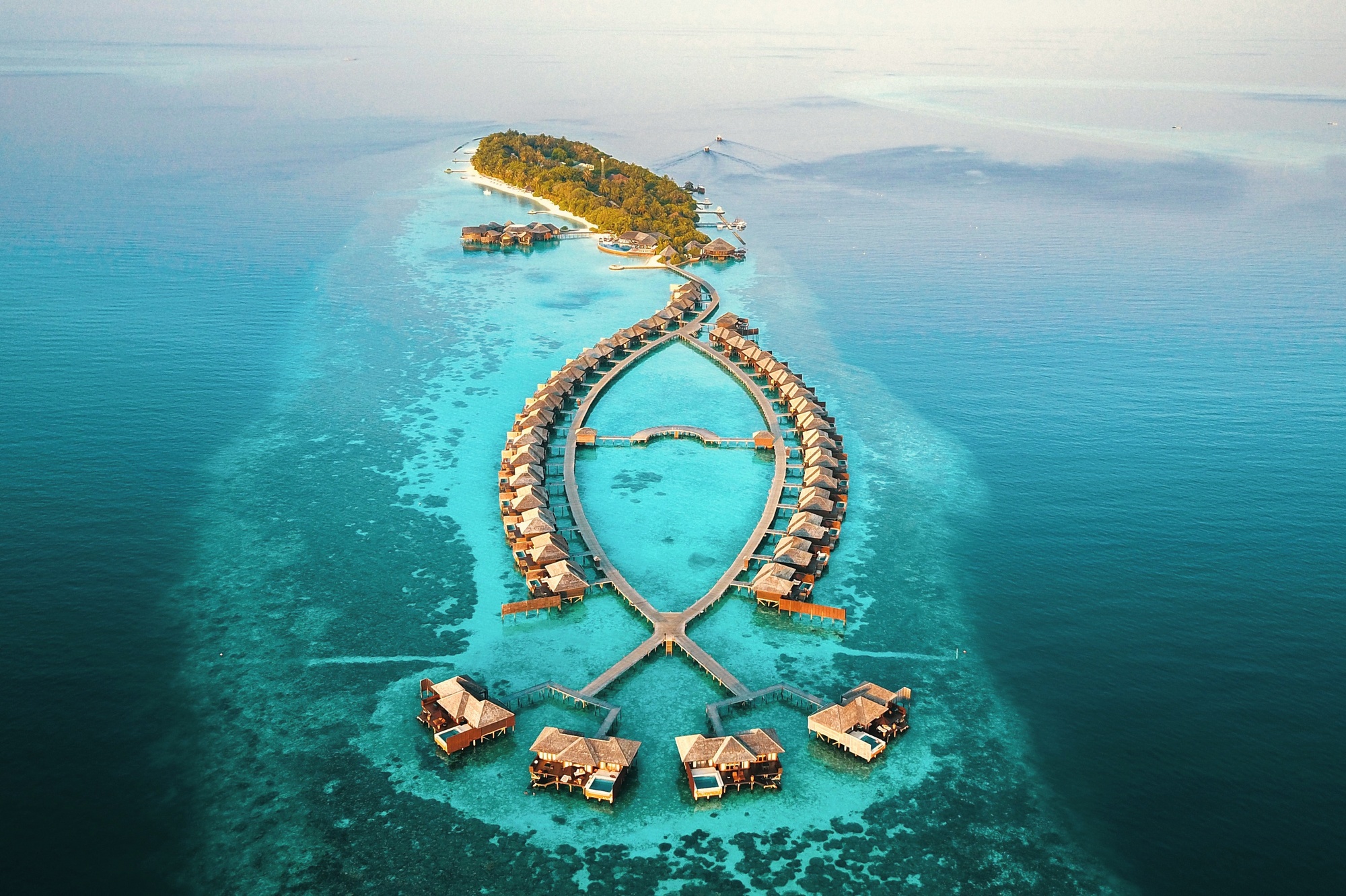 Huvahendhoo from above. The island sits in South Ari Atoll, the reef visible in the shallow water surrounding the property on all sides.