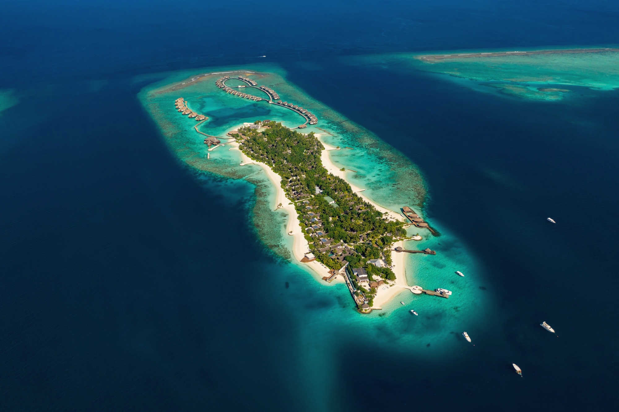 Bolifushi Island from above. The private island sits in South Malé Atoll, ninety villas arranged across beach and overwater positions, twenty minutes by speedboat from Velana.