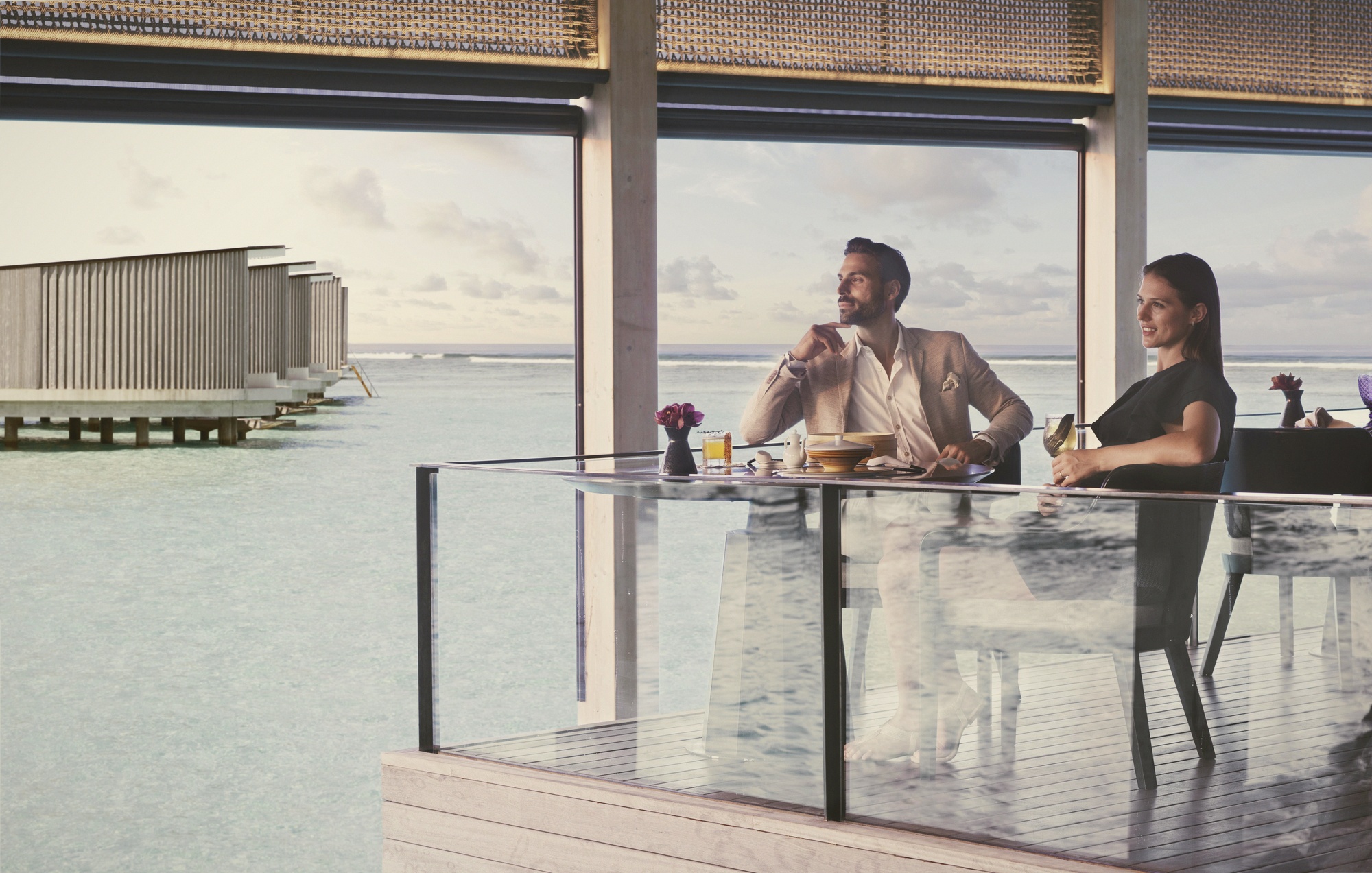 The dining terrace at dusk. The single restaurant operates at the water's edge, with the cove providing a natural windbreak and a consistent quality of evening light.