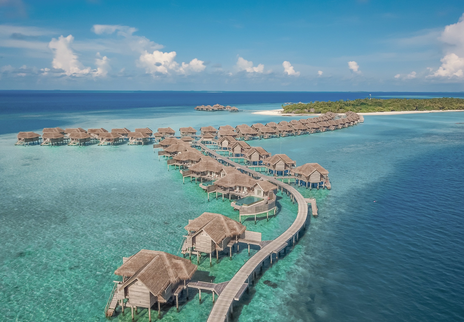 Vakkaru from above: a compact private island in Baa Atoll, ringed by lagoon and dense vegetation, with overwater villas extending from both shores.
